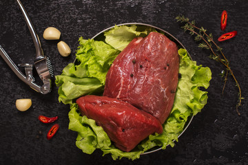 Raw meat with lettuce, garlic, chili peper and thyme over black stone background. Top view....