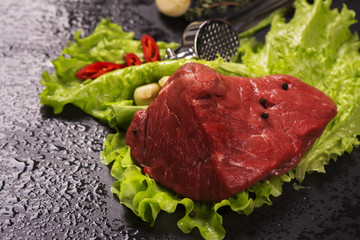 Raw meat with lettuce, garlic, chili peper and thyme over black stone background. Selective focus