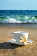 Fototapeta na wymiar white cup with tea or coffee on sand beach front of sea