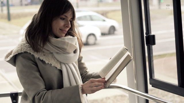 Young, beautiful woman reading book during tram ride
