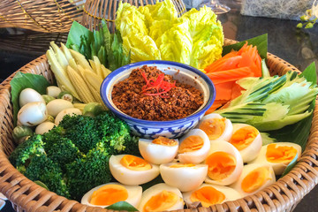 Bowl of Chili Paste with Various Type of Fresh Vegetables and Eggs in Big Rattan Basket for Traditional Thai Style Healthy Meal