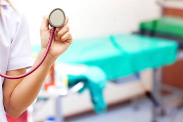 Closeup of medical doctor holding stethoscope towards you.hospital bed background