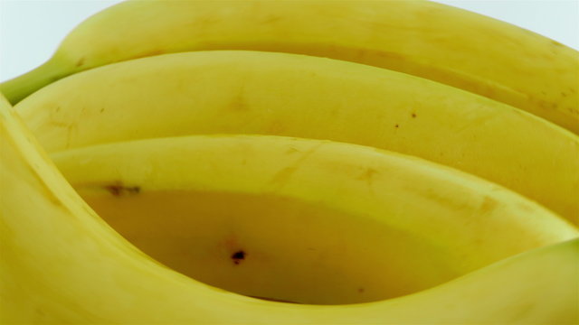 A macro shot of ripe yellow organic bananas rotating against a white background.
