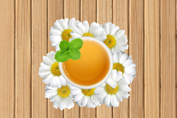 White tea cup with mint on chamomile flowers on wooden texture c