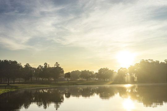Small empty lake river water pond at sunrise sunset dawn early morning dusk with sun rays and trees forest on horizon feeling peaceful relaxed serene calm meditative