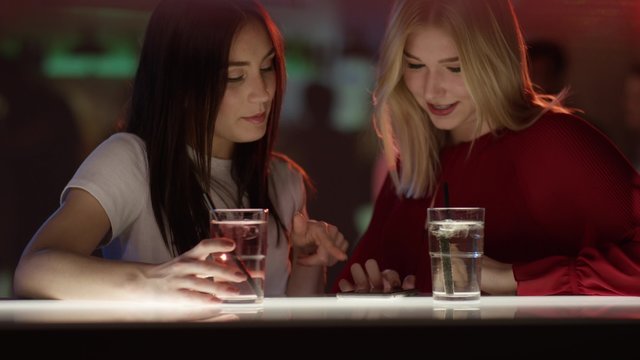 Kichernde M&auml;dchen an Bar mit Handy
