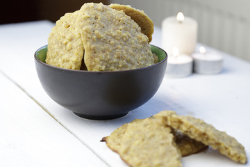 Small brown bowl with home made oat cookies and three candles over a white wooden table