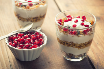 yogurt with homemade granola and pomegranate on the bright wooden board
