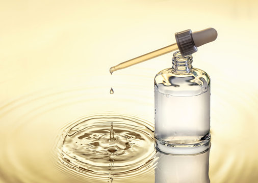 Moisturizing serum for dry skin is standing in the water,  yellow background, pipette with drop, splash.
