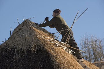 Thatcher working on the ridge of a thatched roof with hazel wood spars