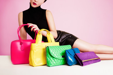 Woman with many colorful bags and purses. Isolated on cute pink color. 