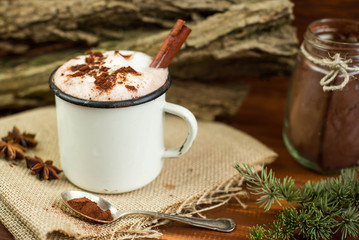 Vintage mug of hot chocolate with cinnamon sticks over rustic background. Kakao powder in vintage spoon. Top view.