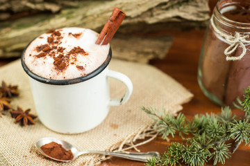 Vintage mug of hot chocolate with cinnamon sticks over rustic background. Kakao powder in vintage spoon. Top view.