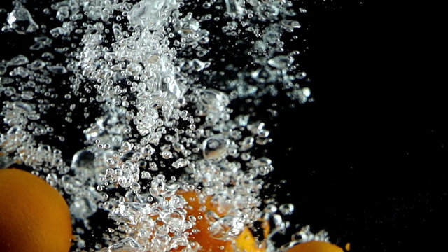 Six tangerines being dropped into water in super slow motion (500 frames per second) against a black background.
