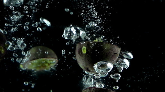 Five passion fruits being dropped into water in super slow motion (500 frames per second) against a black background.
