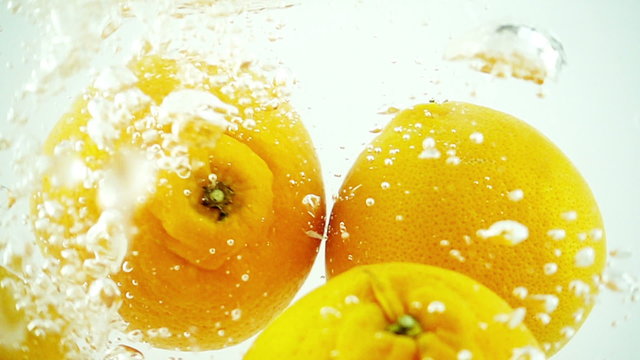 Four oranges being dropped into water in super slow motion (500 frames per second) against a white background.
