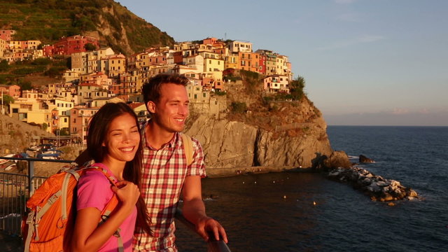 Romantic couple looking at sunset on holidays travel. Young backpacking Asian woman and Caucasian man enjoying ocean view. Young people on vacation in Manarola, Cinque Terre, Liguria, Italy