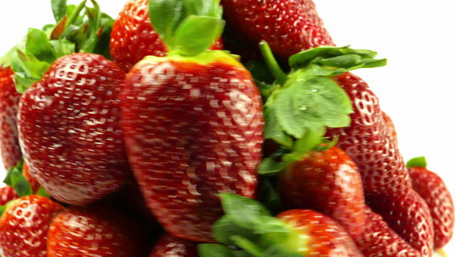 A macro close-up view of a set of fresh strawberries with water droplets revolving around a white background.