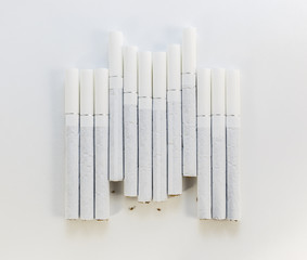 Cigarette with a white filter laid out in a row on a white backg