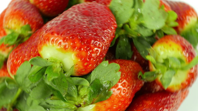 Top-down view of a set of fresh strawberries with water droplets revolving around a white background.
