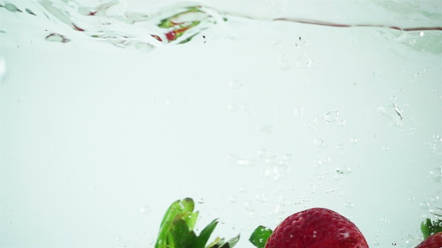 Three large strawberries being dropped into water in super slow motion (500 frames per second) against a white background.
