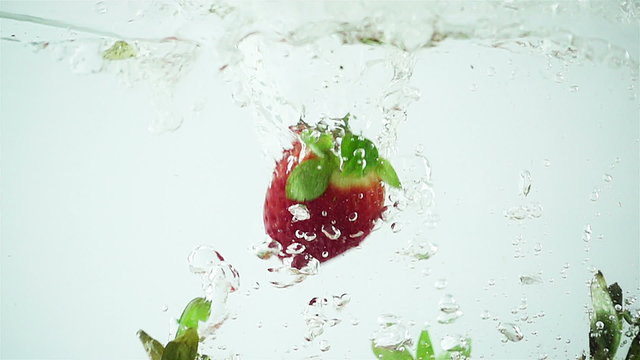 Multiple large strawberries being dropped into water in super slow motion (500 frames per second) against a white background.
