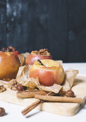 Baked apples with cinnamon sticks and hazelnuts on parchment paper and cutting board on black wooden background