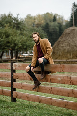 man in a brown coat on a wooden fence