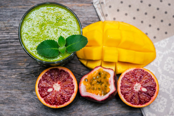 Healthy green smoothie  from spinach, kiwi, pineapple and oranges  with tropical fruits on  wooden table.  Selective focus.