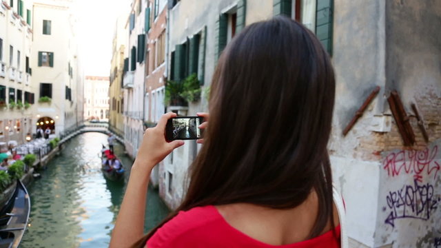 Woman tourist taking picture photo in Venice, Italy. Travel girl using smartphone taking pictures of canal and gondola during vacation holidays in Europe.