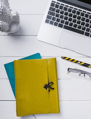 Blue and yellow leather notebook, a pen, glasses and an open notebook on a white background of vintage wooden planks vertical top view without people