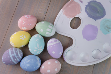 Easter painted eggs on a palette with paints. Light wooden background