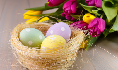 Easter painted eggs in the nest on wooden background with bouguet tulips