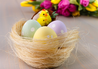 Easter painted eggs in the nest on wooden background with bouguet tulips