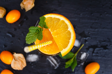 Glass of orange smoothie with ice, peppermint and kumguat on slate plate. Top view.
