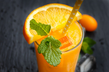 Glass of orange smoothie with ice, peppermint and kumguat on slate plate.