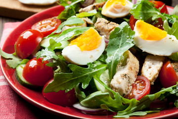 Fresh salad with chicken, tomatoes, eggs and arugula on plate