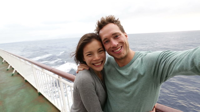 Cruise ship couple taking selfie self portrait photo romantic. Happy lovers, woman and man traveling on vacation travel sailing on open sea ocean enjoying romance. Young Asian woman and Caucasian man.