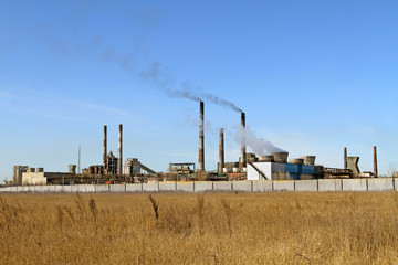 Fototapeta na wymiar Yellow steppe and factory with smoking chimneys against the blue