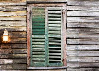Old rustic vintage dilapidated antique house home building structure with green window shutters closed and porch light lantern glowing turned on - 103214174