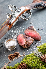 deer or venison steak with antique long gun and ingredients like sea salt and pepper, food background for restaurant or hunting loving