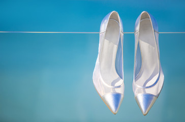 Elegant woman's silver wedding shoes on blue sea background