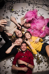 Cheerful friends lying on the floor in nightclub and making selfie