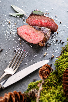 deer or venison steak with ingredients like sea salt, herbs and pepper and cutlery, food background for restaurant or hunting loving