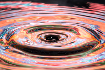 Single solitary drip drop of water into colorful reflective calm puddle pool creating ripples waves rings circles movement - 103216538