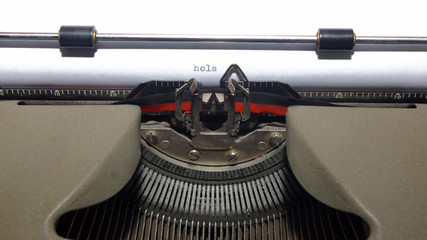 HOLA (Hello in Spanish language). Message written on old typewriter on white paper © alejomiranda