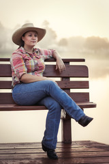 Girl woman lady female caucasian with long dark brown hair sitting on wood bench on foggy lake pond dock in cowboy hat flannel shirt looking relaxed happy serene beautiful young peaceful