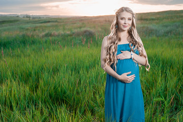 Beautiful tender pregnant woman standing on green grass and looking at the camera