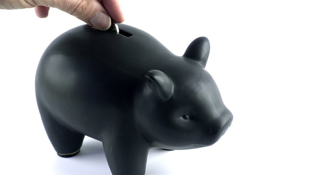 Saving up for the future: a young male inserting British pounds in a black piggybank against a white background.
