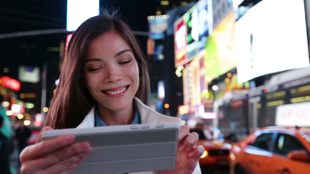 Tablet computer - woman using app in New York City, Time Square, Manhattan. Girl tourist or New Yorker on small tablet pc at night. Lifestyle video with beautiful multiracial woman in her 20s.